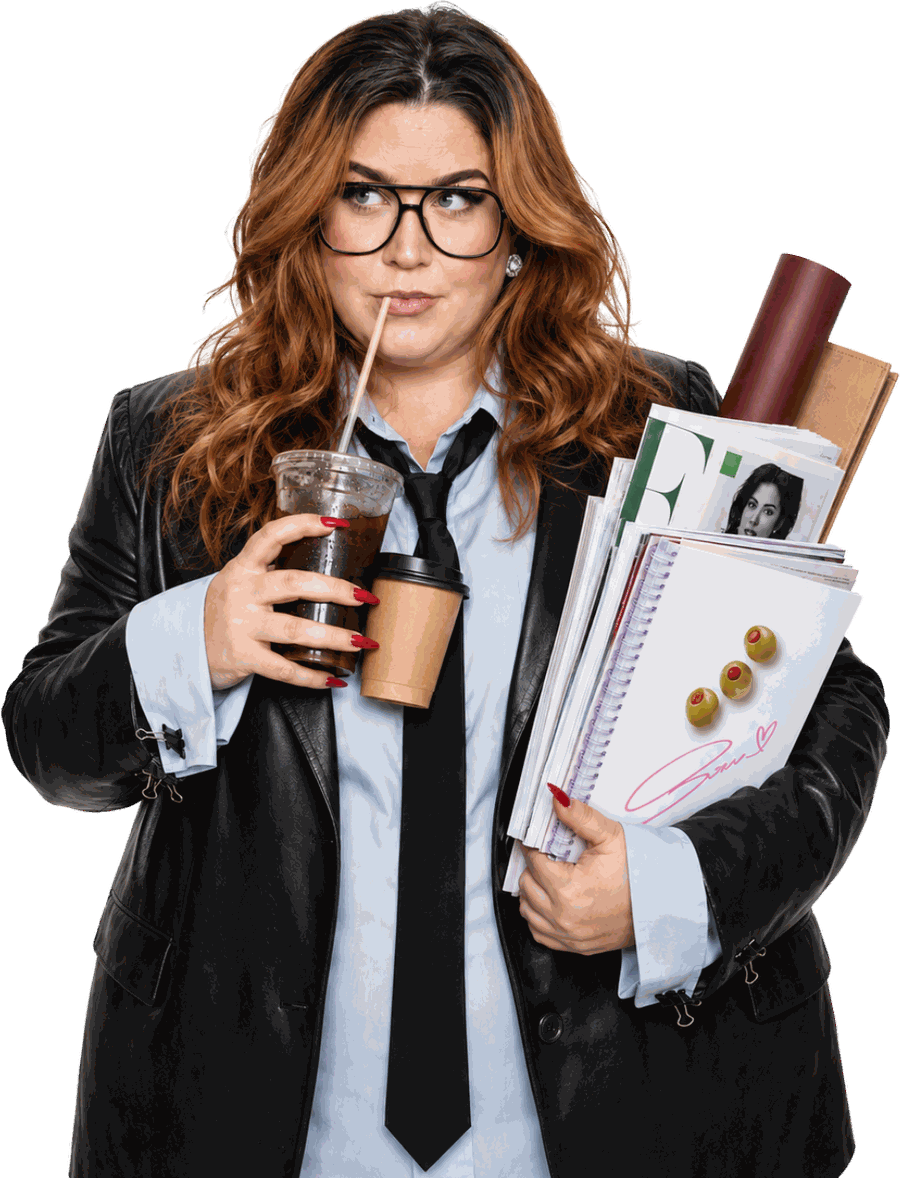Allie Fern in a leather blazer and loose tie, drinking an iced coffee with an armful of magazines and papers